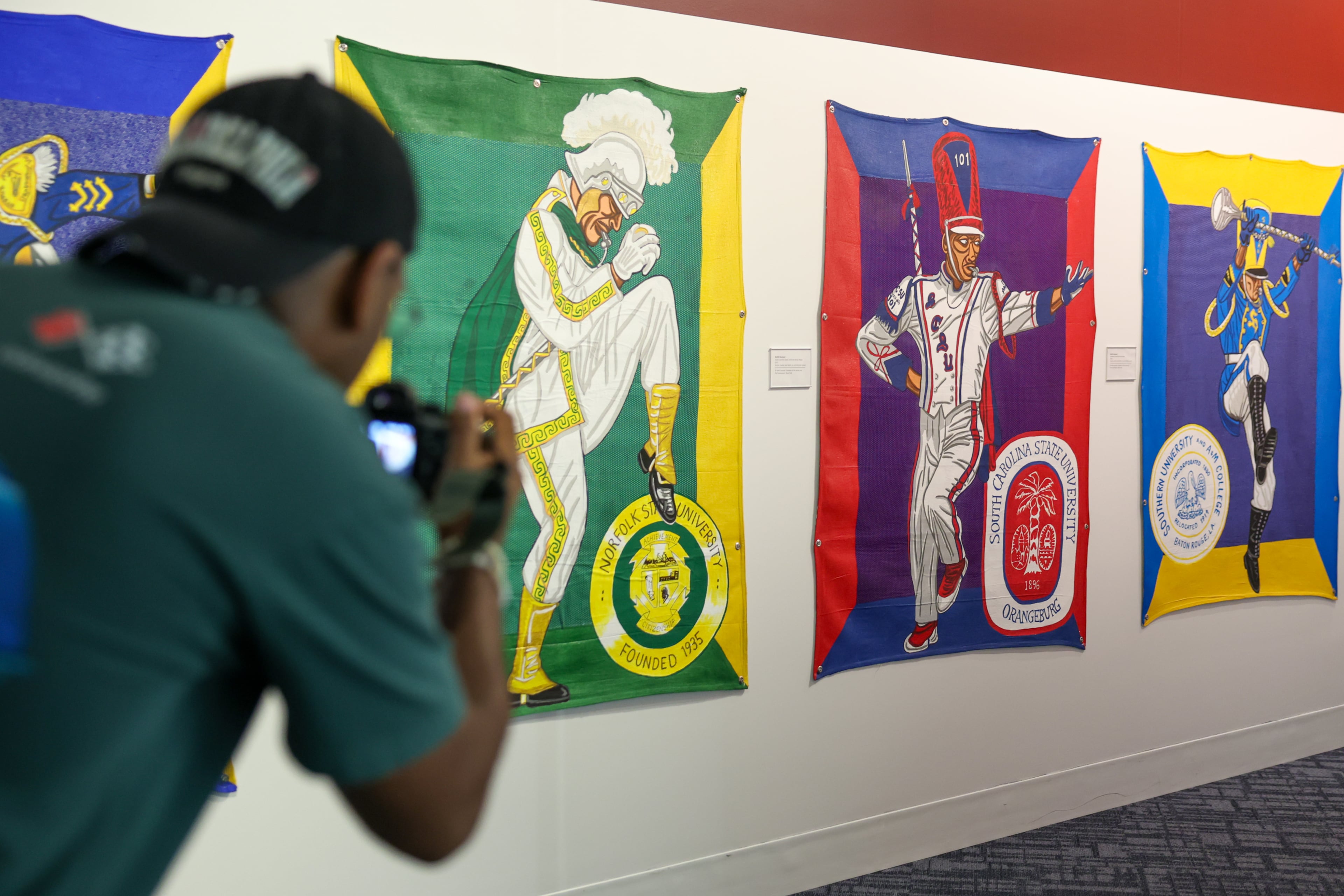 Joshua Owens takes photos of artist Keith Duncan’s exhibit “Battle of the Bands,” inspired by HBCU band culture, at the College Football Hall of Fame in Atlanta on Sept. 11, 2026. Duncan utilizes bright colors to convey the competition and pageantry between the bands. (Arvin Temkar/AJC)