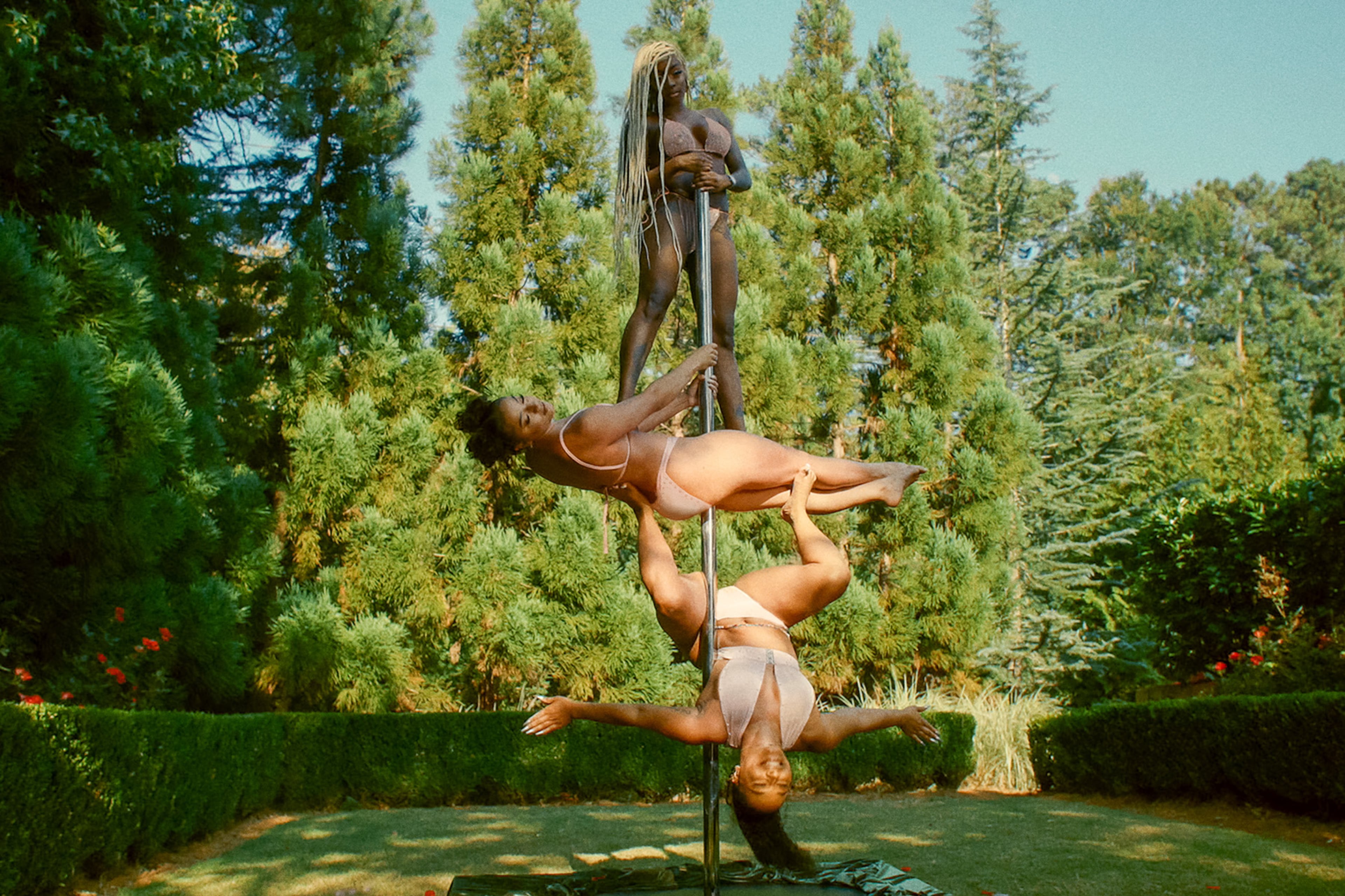 Three Magic City dancers strike balancing poses while supporting each other on a pole in an undisclosed outdoor area. (Courtesy of Starz)