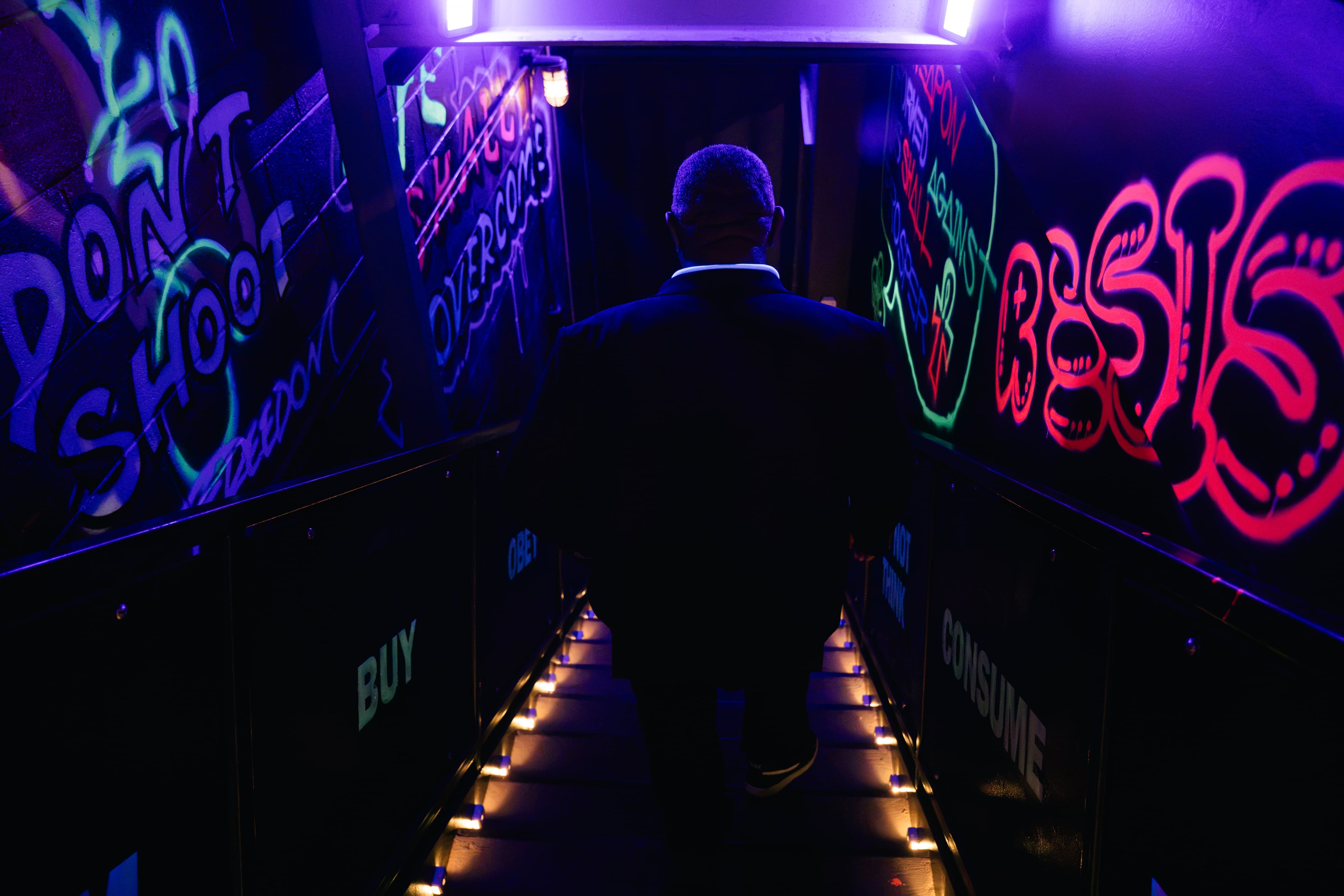 A visitor walks down a staircase surrounded in neon graffiti while leaving “Mothership Sirius B” during a preview of the exhibit on Aug. 12, 2026, in Atlanta. The neon messages throughout the staircase offer cultural commentary as visitors exit the immersive experience. (Olivia Bowdoin/AJC)