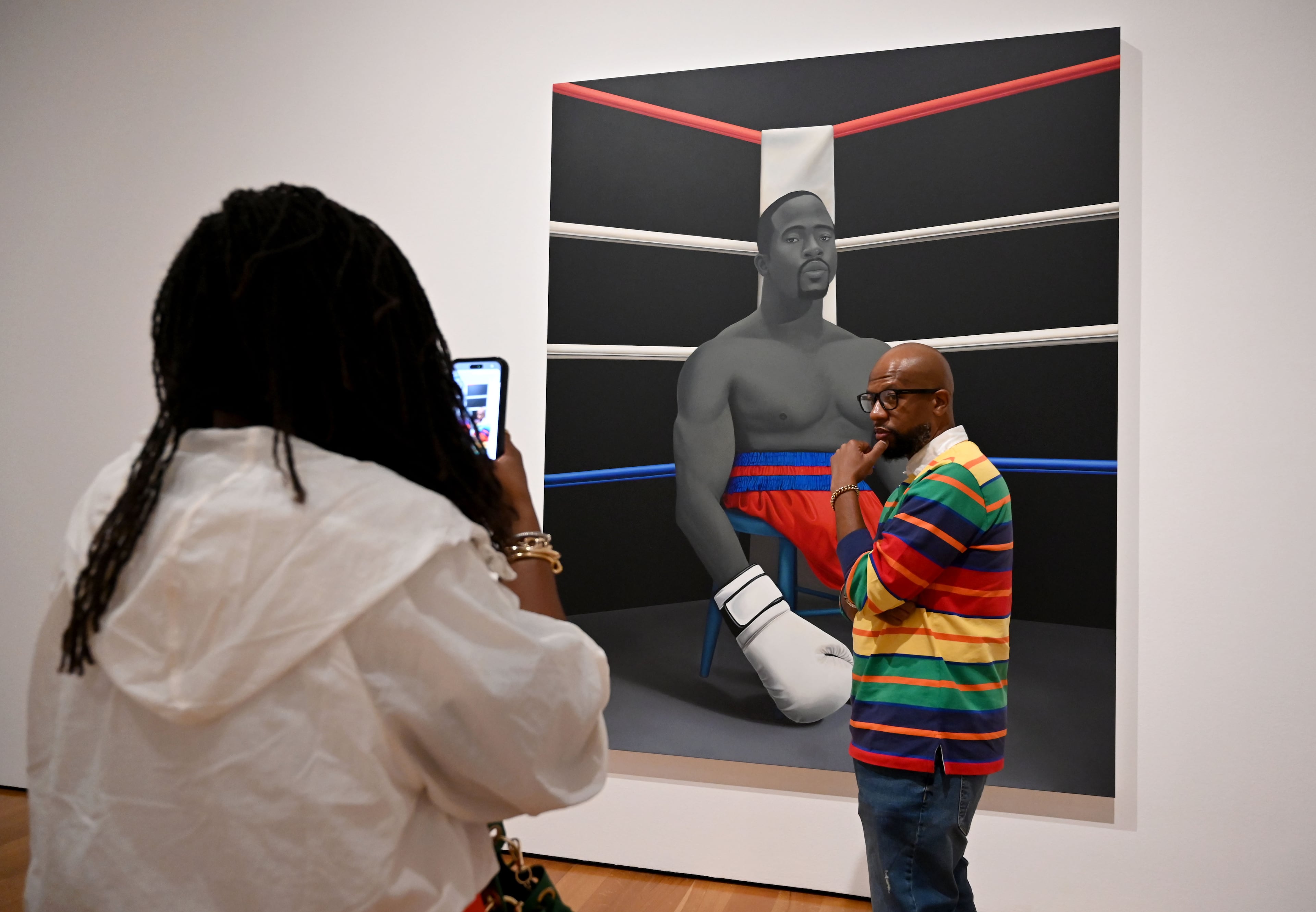 Jodian White (left) takes a picture of her husband Vernon White in front of "American Grit" at Georgia-born Amy Sherald’s “American Sublime” exhibition at the High Museum of Art on Friday, May 15, 2026, in Atlanta. (Hyosub Shin/AJC)