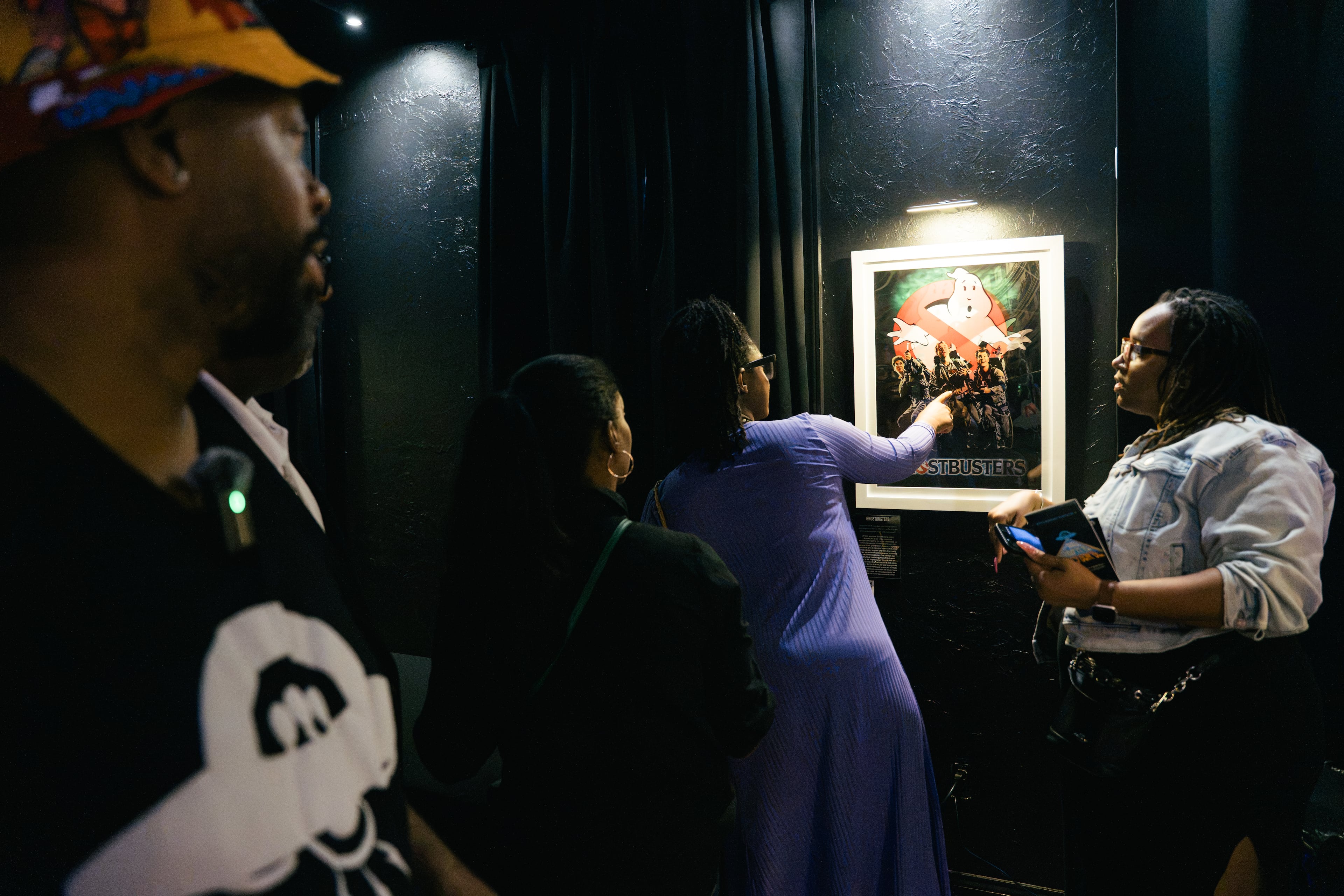 Visitors view artist Fabian Williams’ reimagined “Ghostbusters” poster while Williams, left, answers questions during a preview of “Mothership Sirius B” on Aug. 12, 2026, in Atlanta. The exhibit uses familiar science-fiction imagery to examine ideas about the past, present and future. (Olivia Bowdoin/AJC)