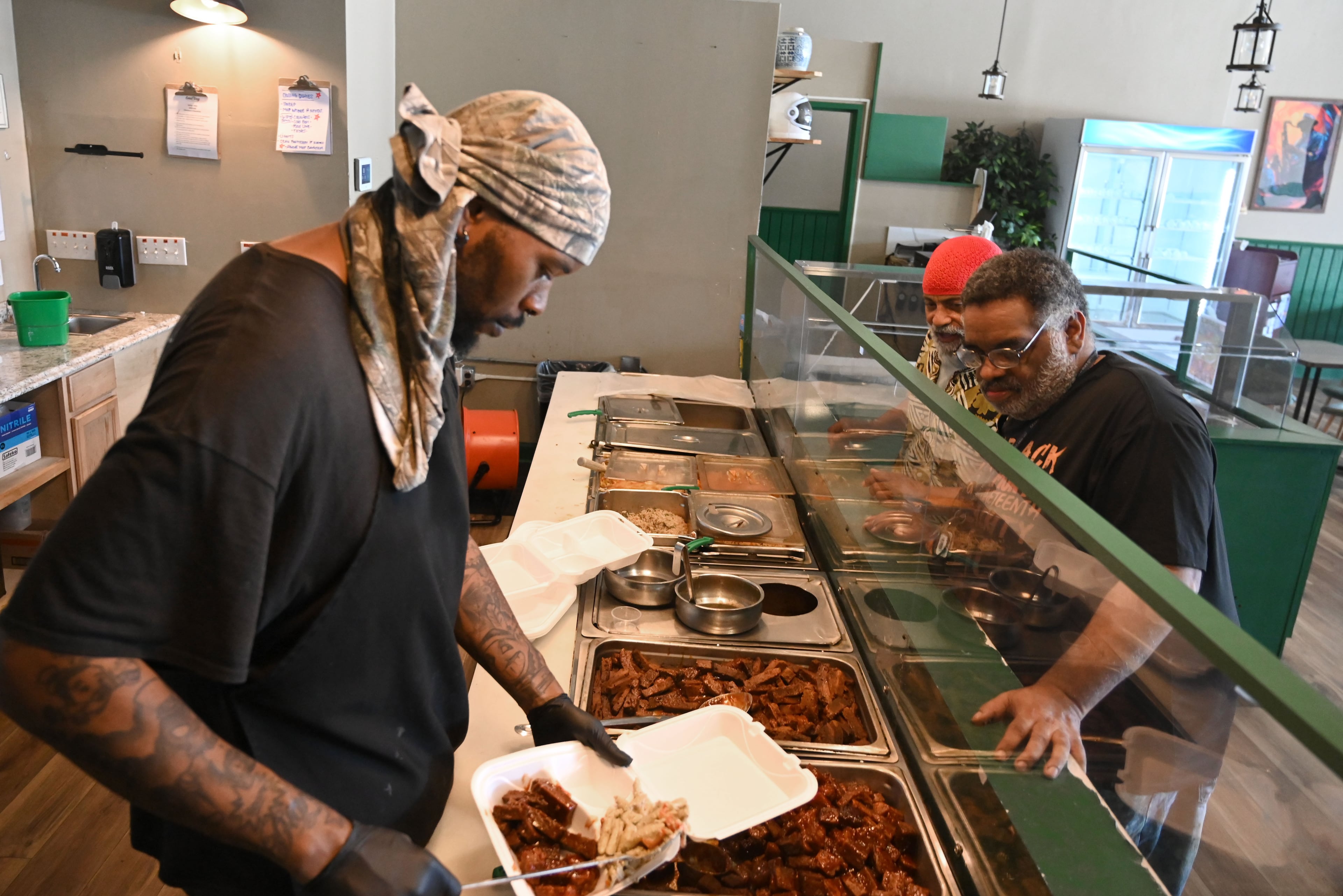 Marvin Griffin, left, serves a customer as St. Micael Shaleahh, background, one of the restaurant's original co-owners, greets the customer at The New Soul Veg on Thursday, July 9, 2026, in Atlanta. (Hyosub Shin/AJC)
