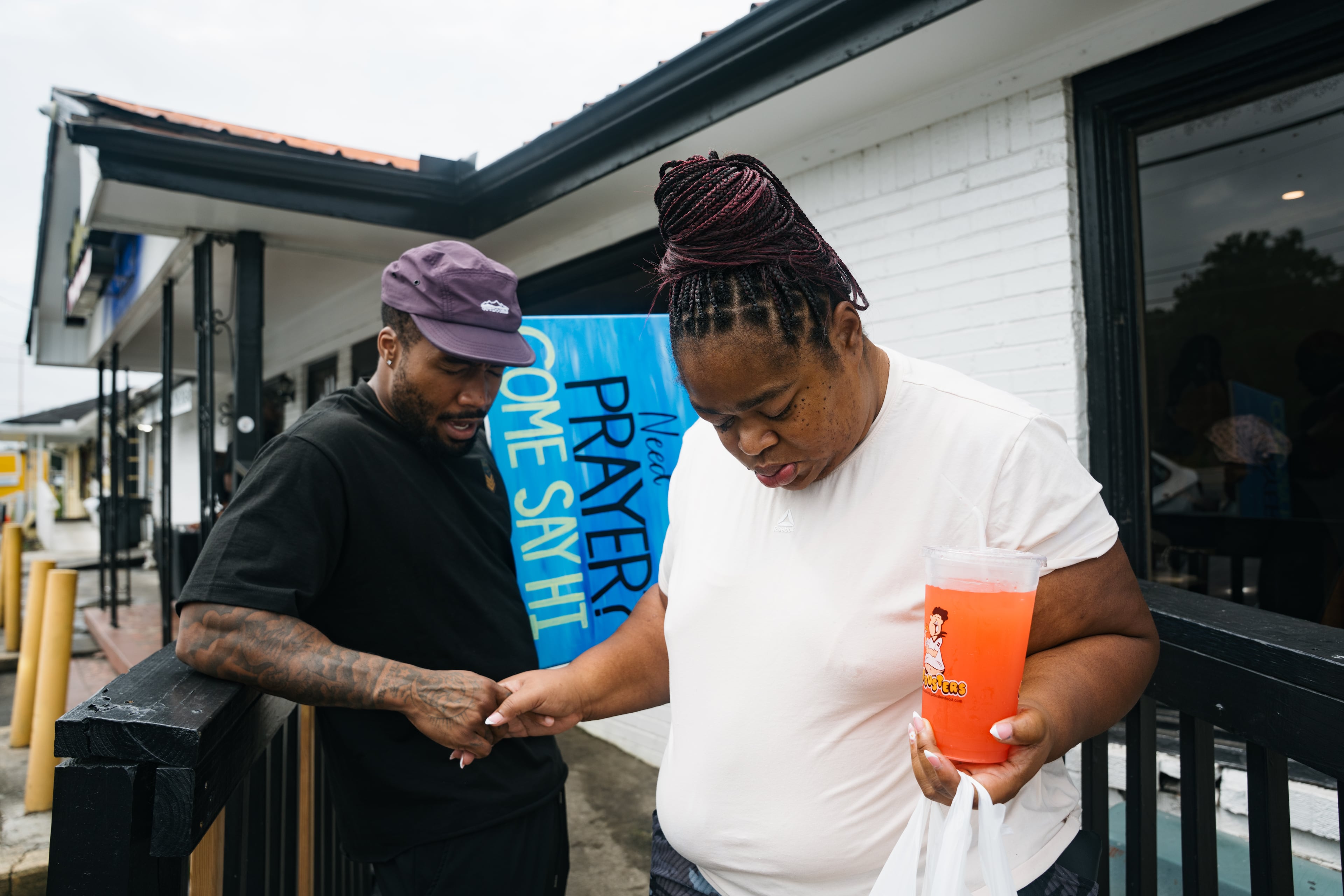 Volunteer Josh Alexander (left) prays with a customer as she leaves Gutbusters restaurant during the Bloom outreach event Saturday, July 25, 2026, in Decatur. (Olivia Bowdoin for the AJC)
