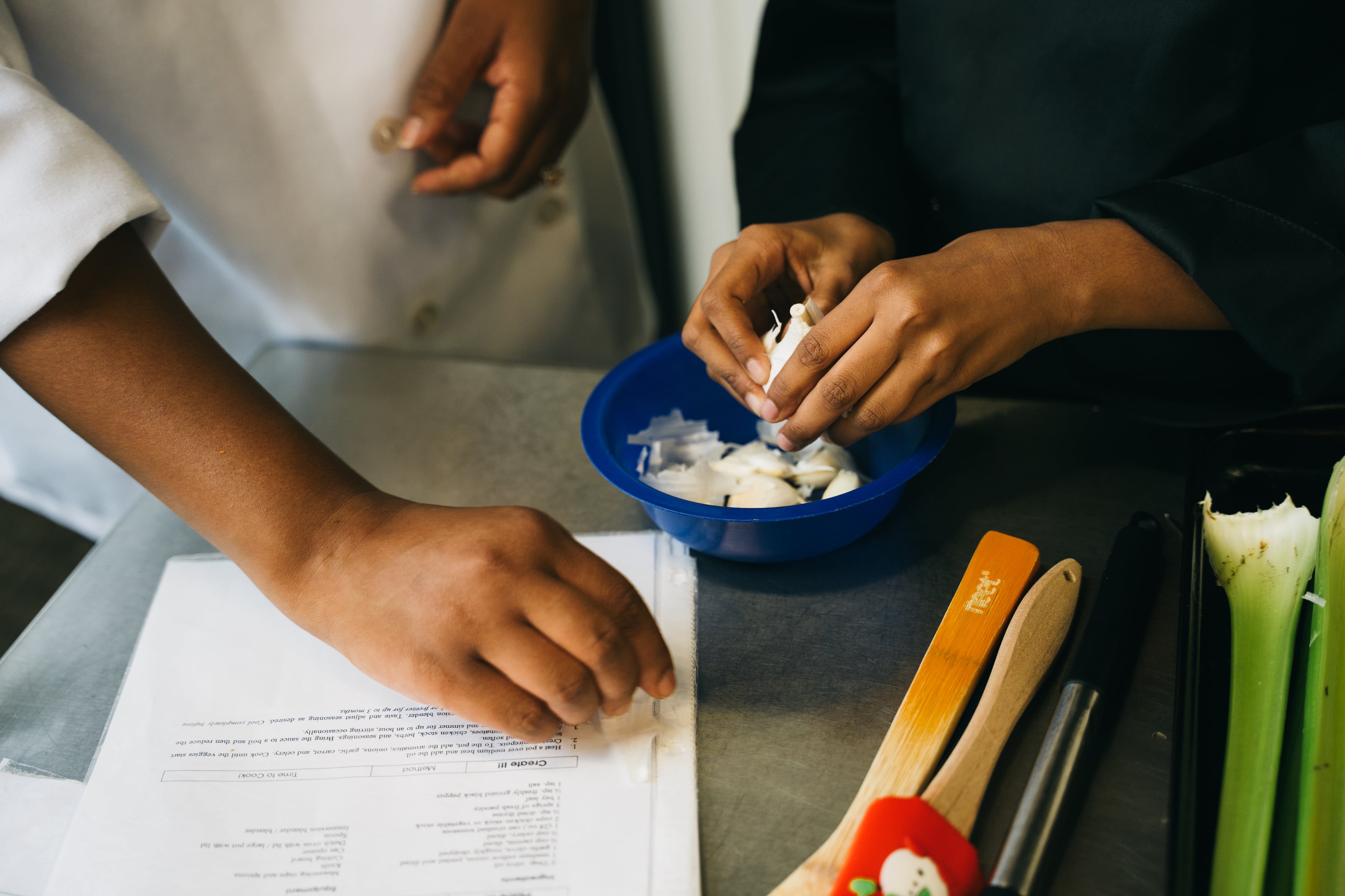 Chef Arielle Jolly-Williams, left, teaches 11-year-old Dhyanaa Satish Kumar, right, to peel a garlic clove in the Young Chefs Academy kitchen in Sandy Springs on Friday, Aug. 28, 2026. (Olivia Bowdoin for the AJC)