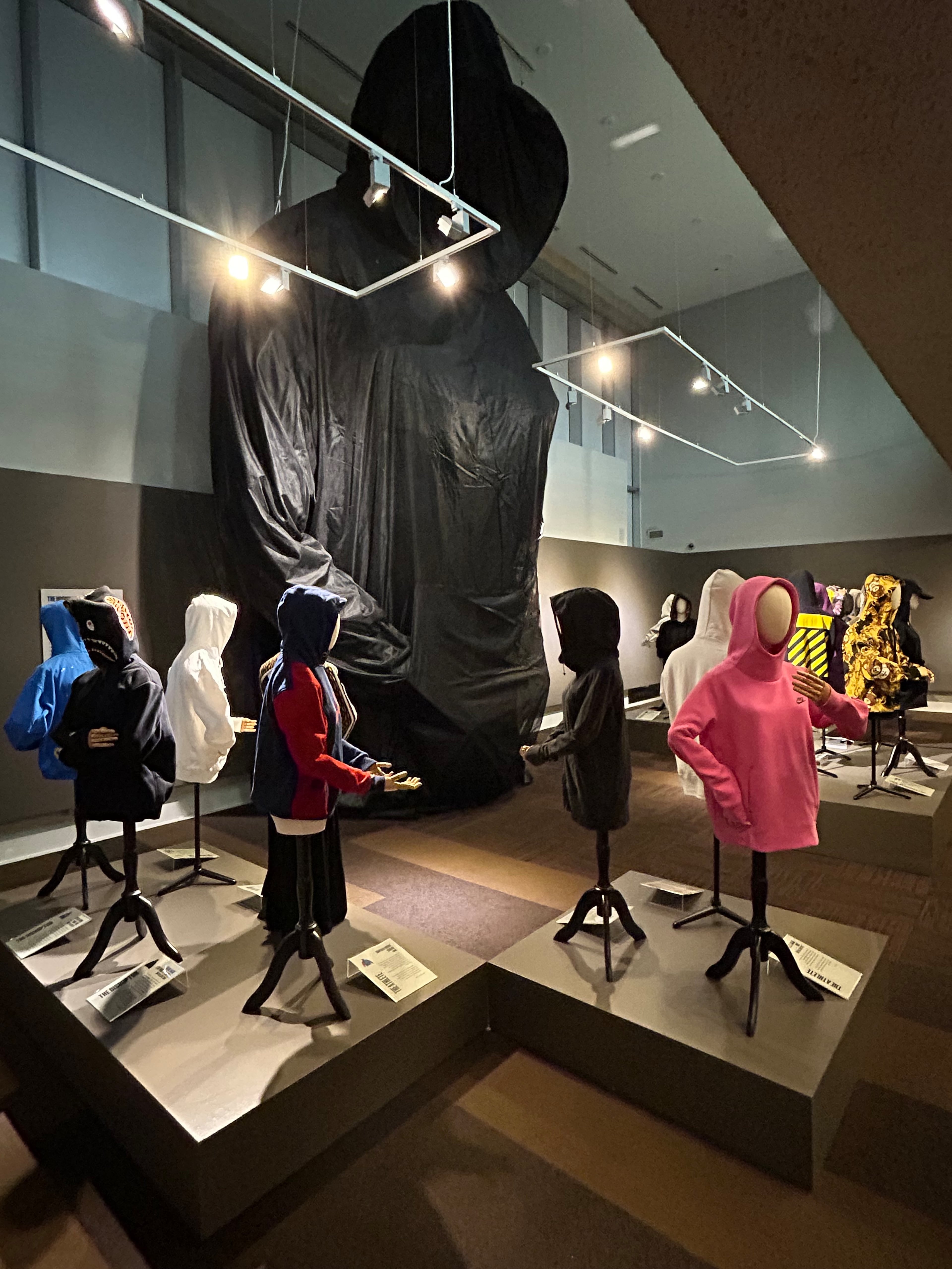Hoodies from "The Hoodie" exhibit at MODA are displayed in front of a 26-foot-tall sculpture of a hoodie-wearing figure. (Photo by Susan Sanders)