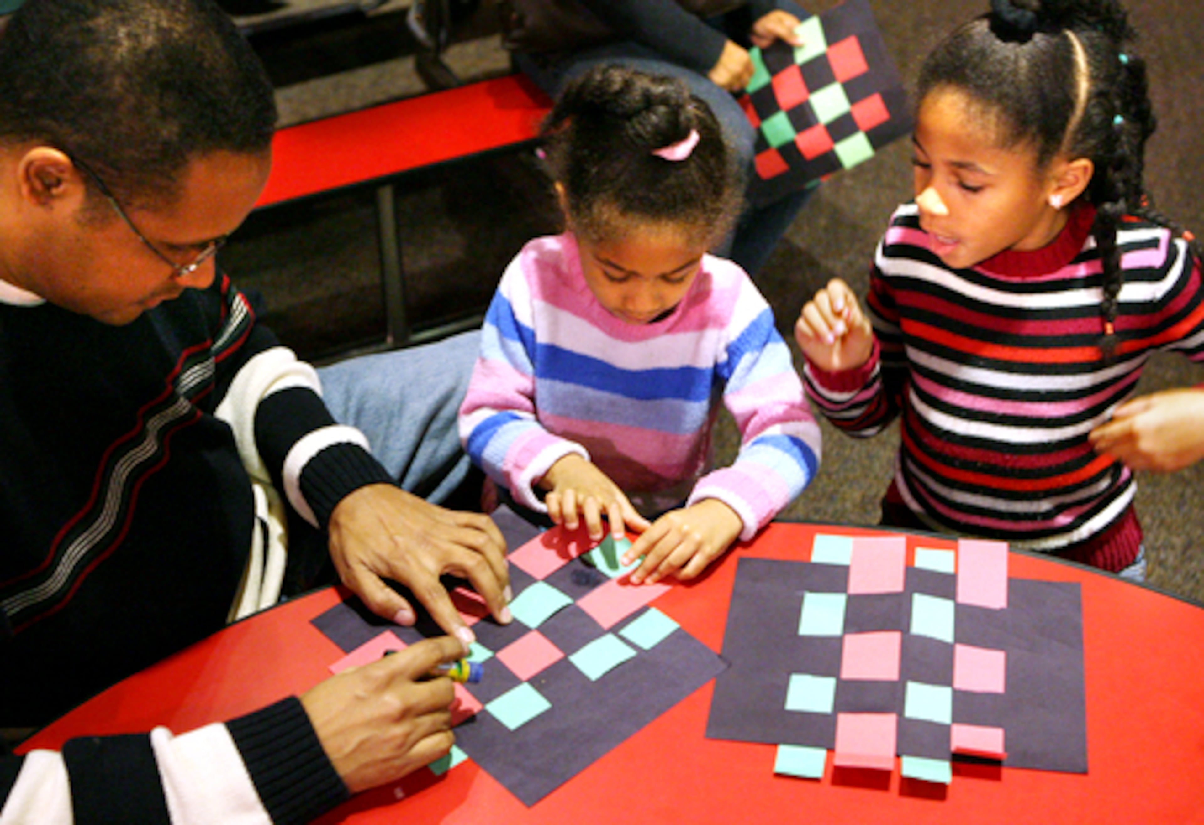 Angel DeLaCruz helps his daughters Gabriella, 4, center, and Jordan, 6, make Kwanzaa mats at Imagine It! The Children's Museum of Atlanta. The "make-and-take" activity was part of a Kwanzaa event at the center.(AJC File)