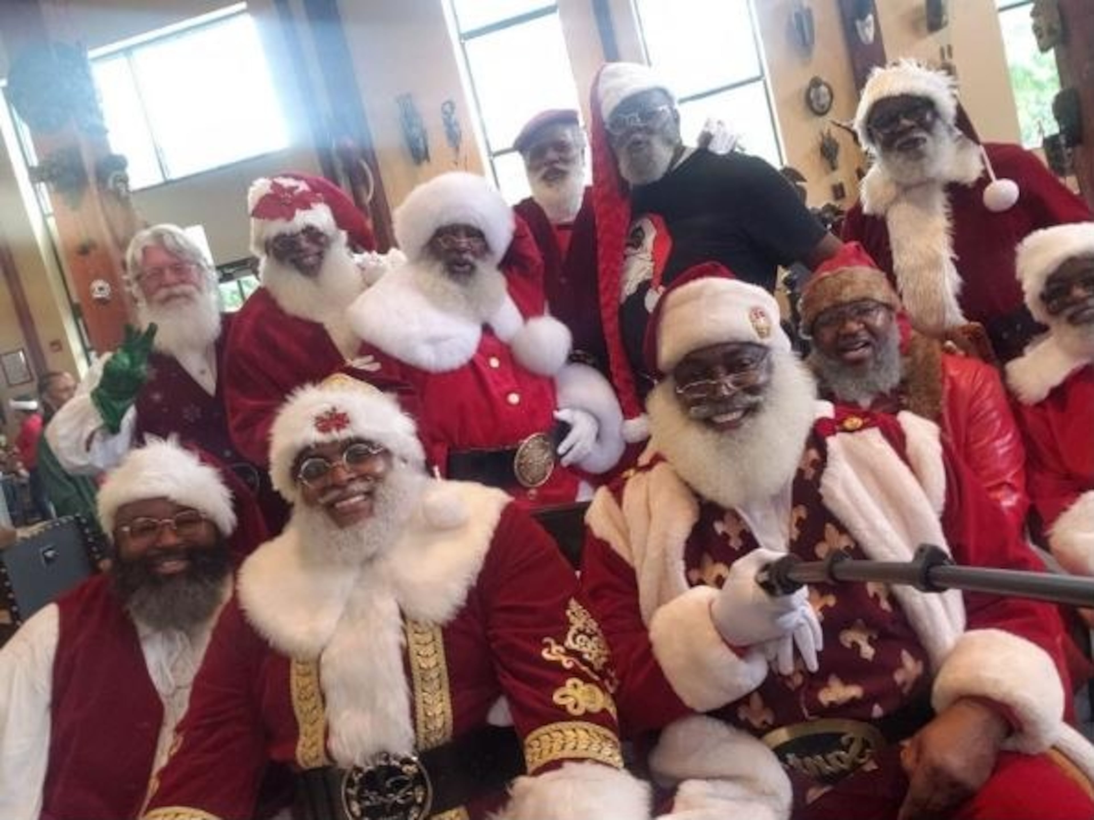 A group photo of a gathering of Santas of Color Coalition, led by Dion Sinclair, a.k.a. "The Real Black Santa," holding a selfie stick.
